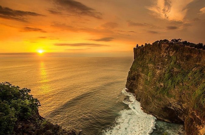 A headland on the Bukit with the sun setting behind it over open water