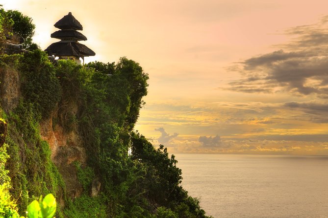 Uluwatu's thatched meru roofs against a pale evening sky above the sea